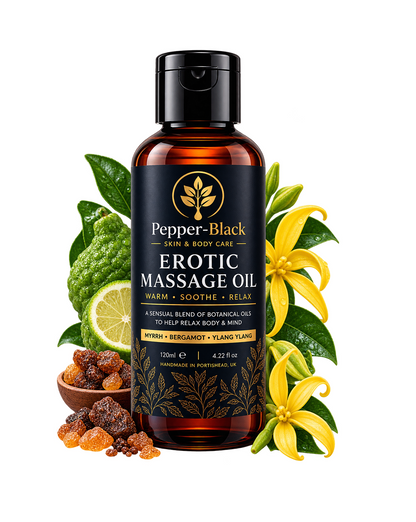 A bottle of Pepper-Black Erotic Massage Oil centered on a white background, surrounded by botanical ingredients including yellow flowers, green leaves, a lime slice, and dried fruits in a small wooden bowl.